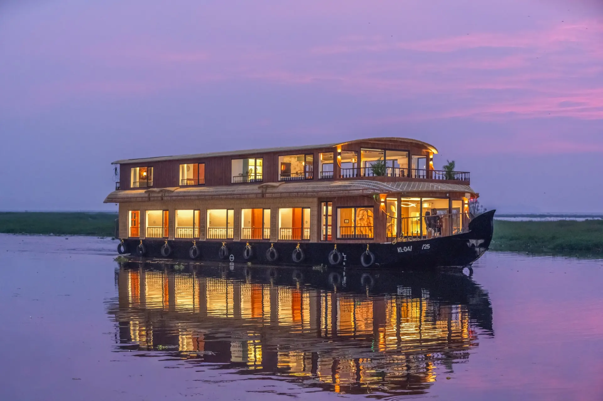 Luxury Kerala houseboat exterior at twilight with glowing interiors